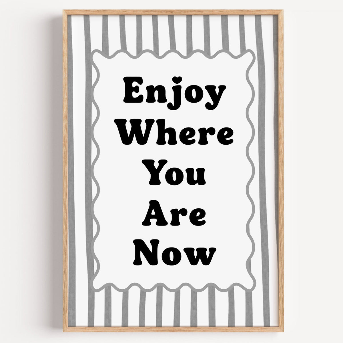 Enjoy where you are now striped quote print in a light oak frame on a plain white wall