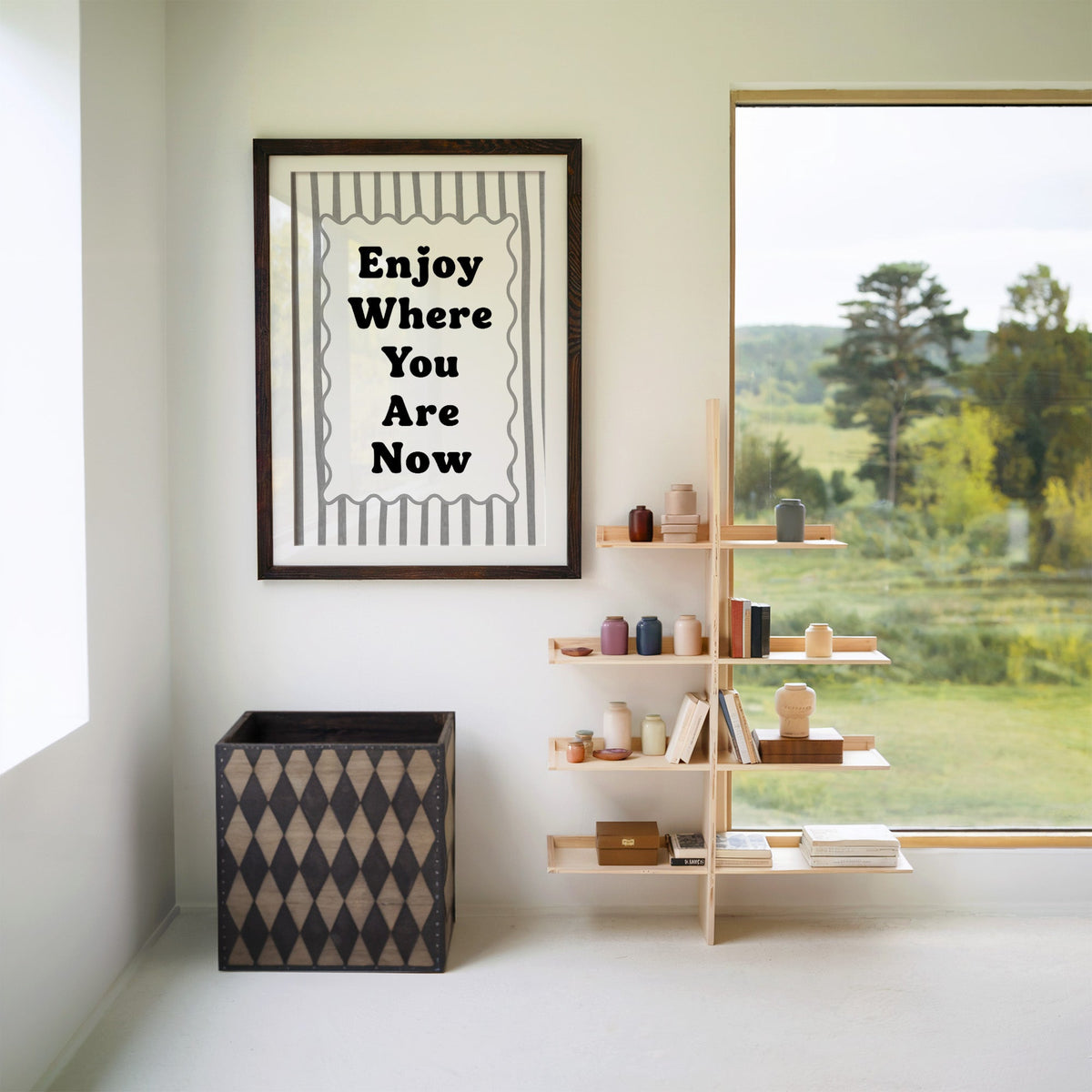 Enjoy where you are now striped quote print in a walnut frame with a white mat beside wooden shelves and a garden window