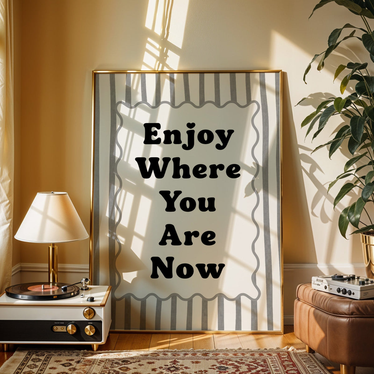 Enjoy where you are now striped quote print shown in a gold frame beside a record player and table lamp