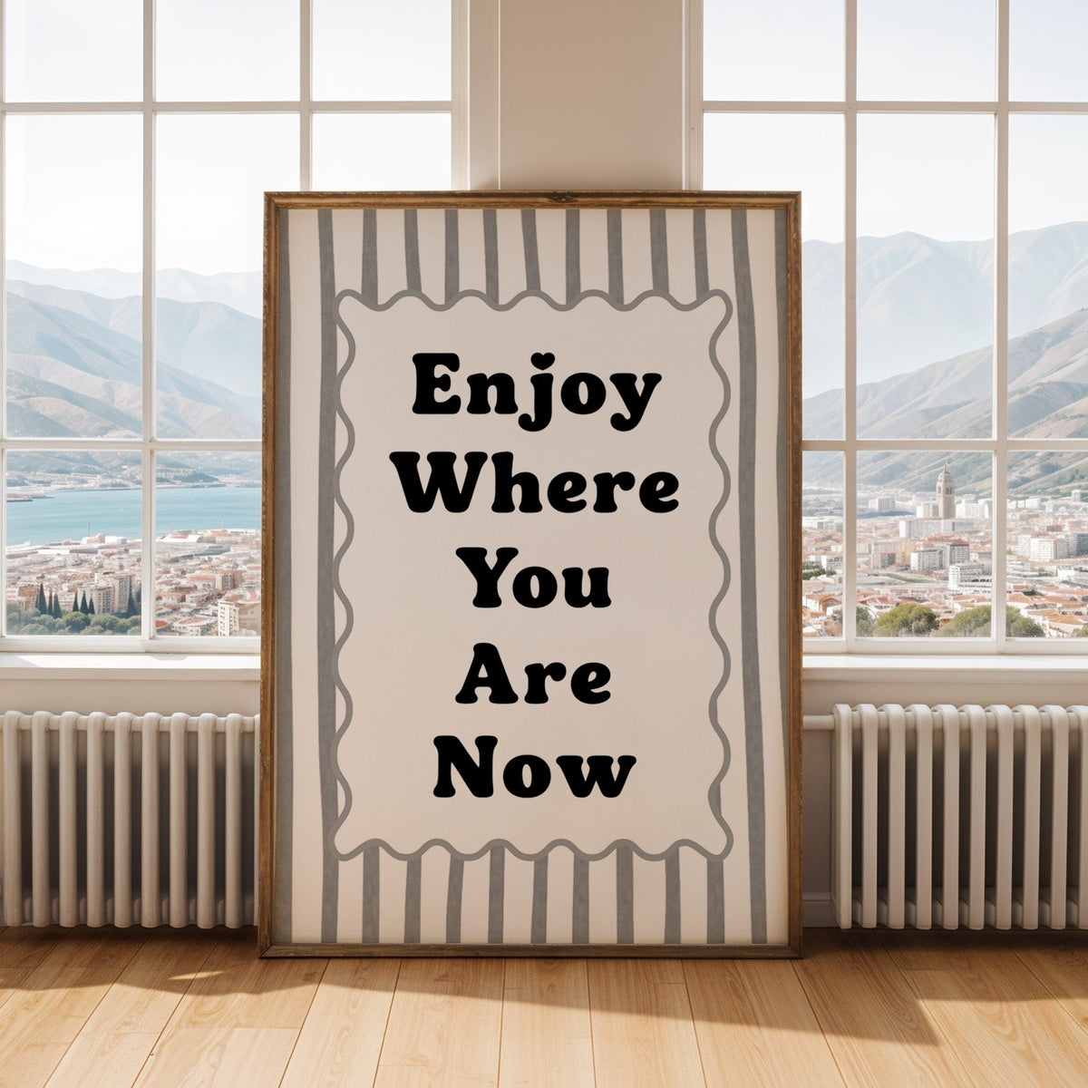 Enjoy where you are now striped quote print shown in an antique gold frame by tall windows with a sea view