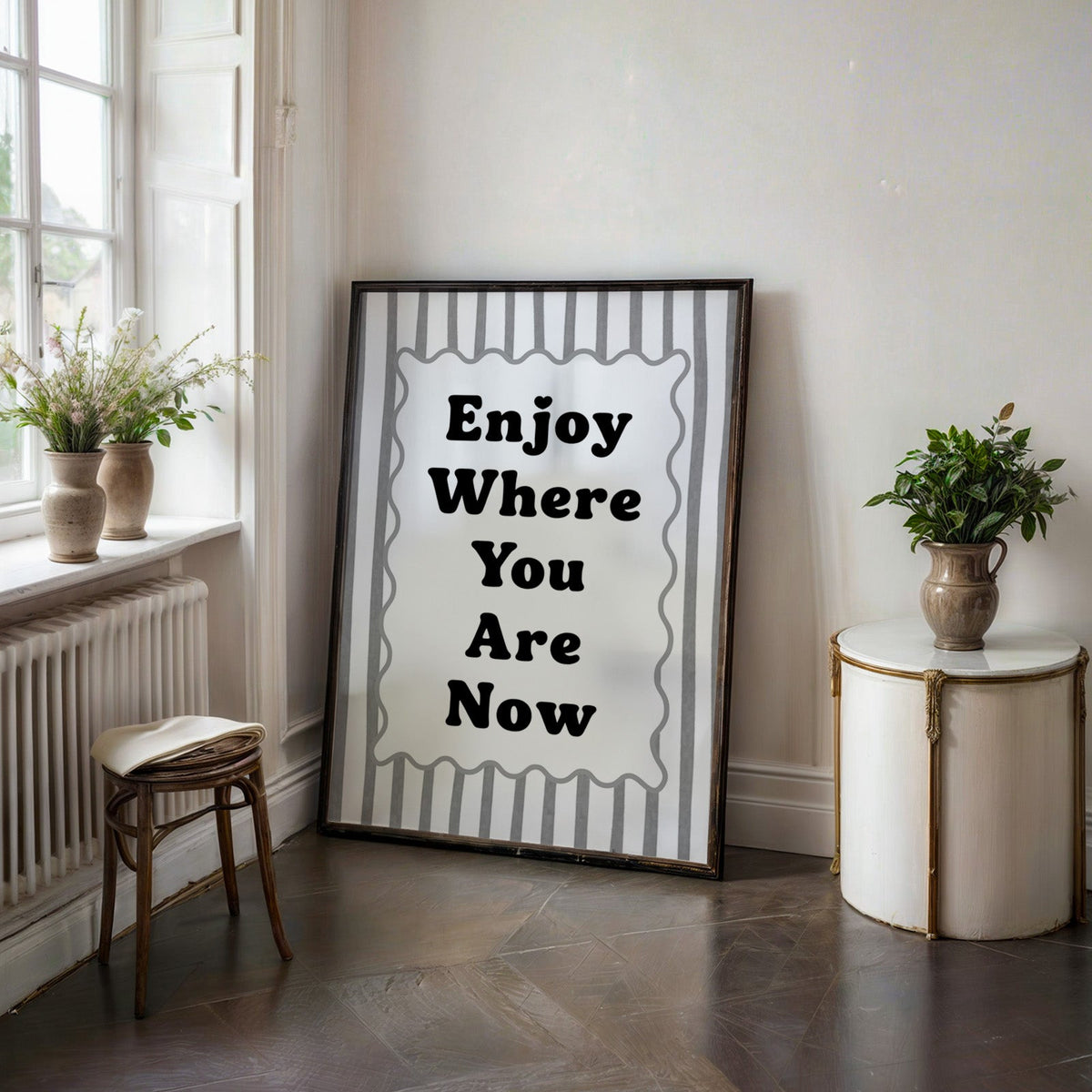 Enjoy where you are now striped quote print in a black frame on a dark stone floor beside a white side table