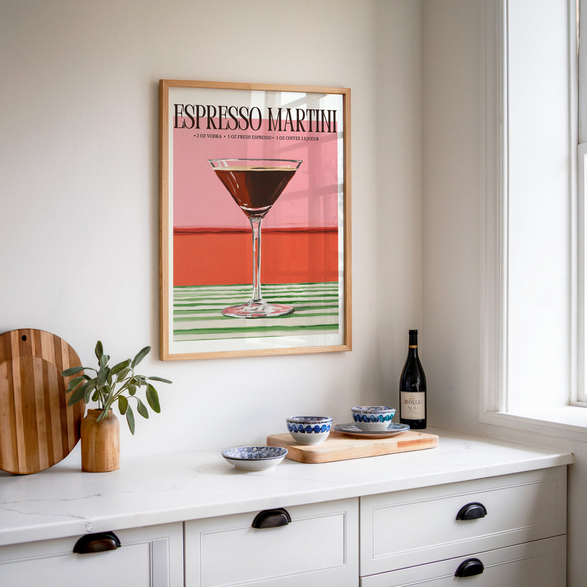 Espresso martini recipe print in an oak frame above a white sideboard with a bottle of wine