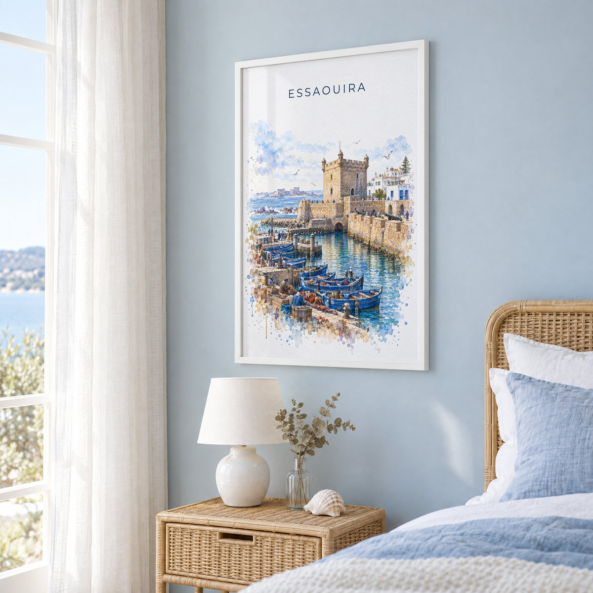 Essaouira watercolor print in a white frame on a pale blue wall beside a rattan bed in a coastal bedroom