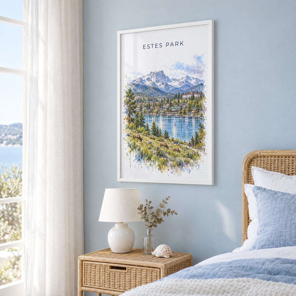 Estes Park watercolor print in a white frame on a pale blue wall beside a rattan bed in a coastal bedroom