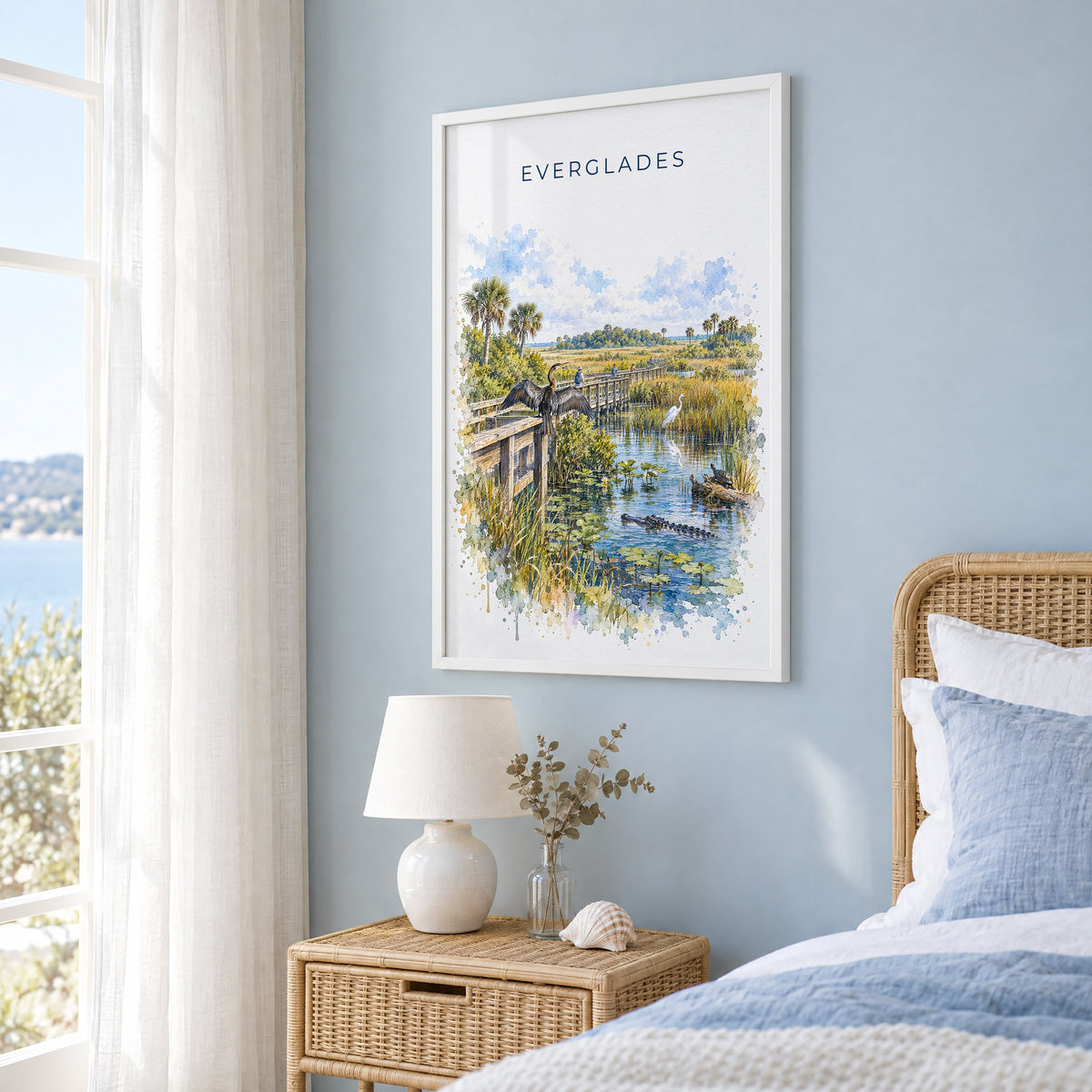 Everglades National Park watercolor print in a white frame on a pale blue wall beside a rattan bed in a coastal bedroom