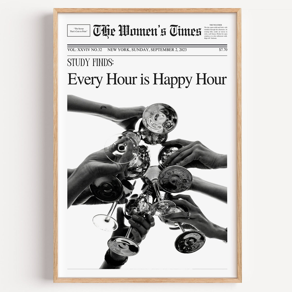 Mock front page with hands toasting cocktail glasses print in a light oak frame on a plain white wall