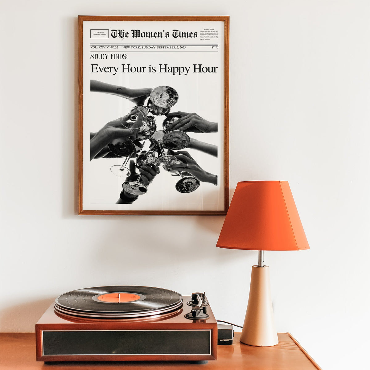 Mock front page with hands toasting cocktail glasses print in a walnut frame above a record player and orange lamp