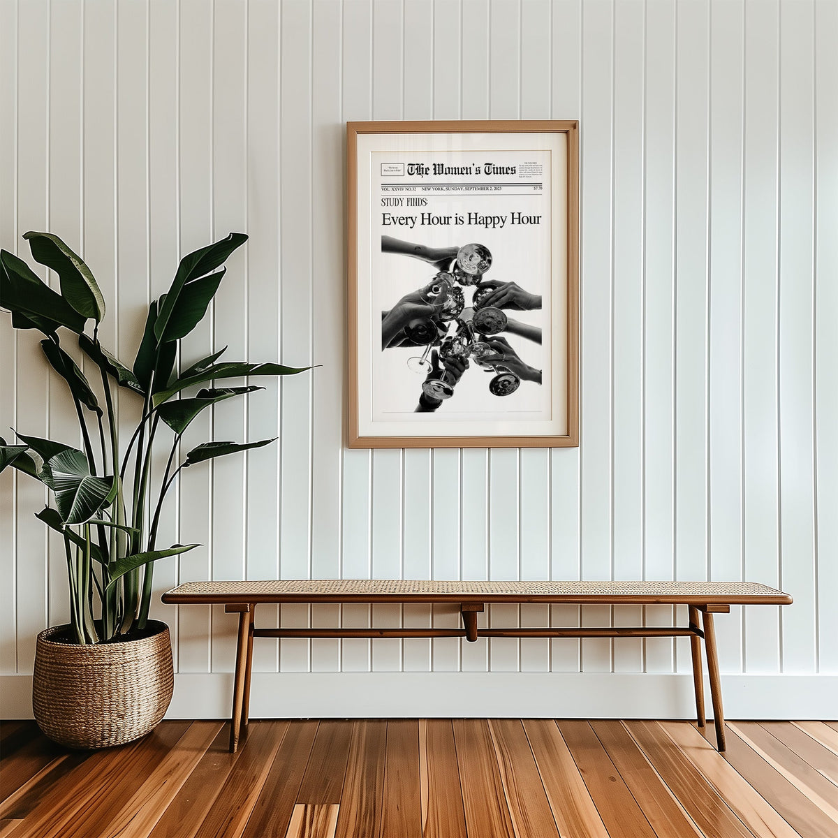 Mock front page with hands toasting cocktail glasses print in a wood frame with a white mat above a cane bench