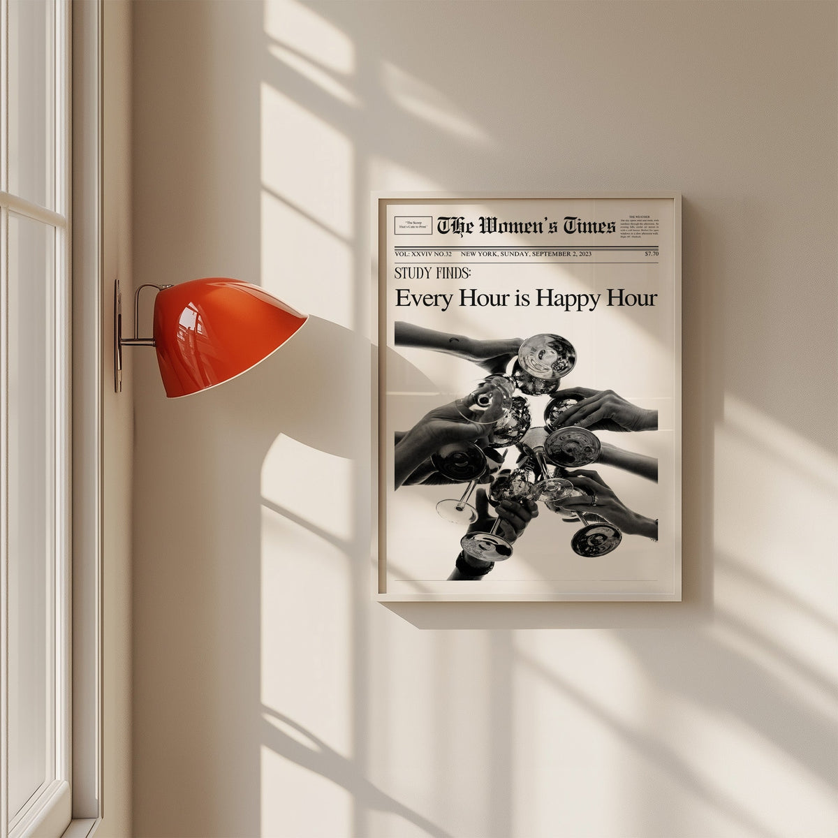 Mock front page with hands toasting cocktail glasses print in a white frame on a sunlit wall beside a red sconce