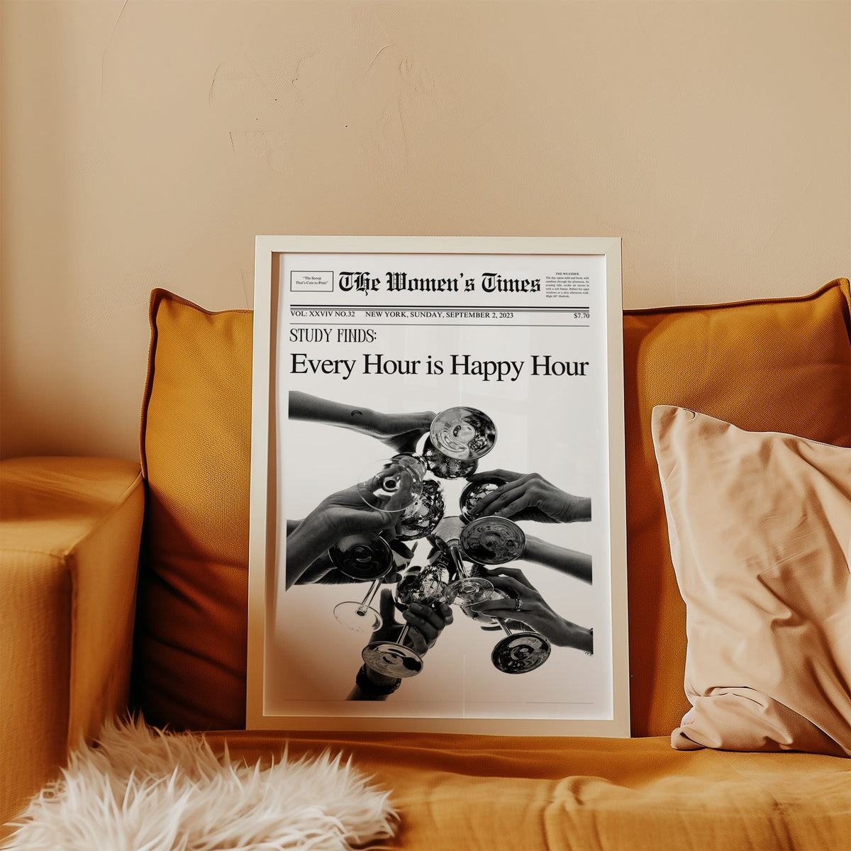 Mock front page with hands toasting cocktail glasses print in a white frame leaning on a mustard velvet sofa