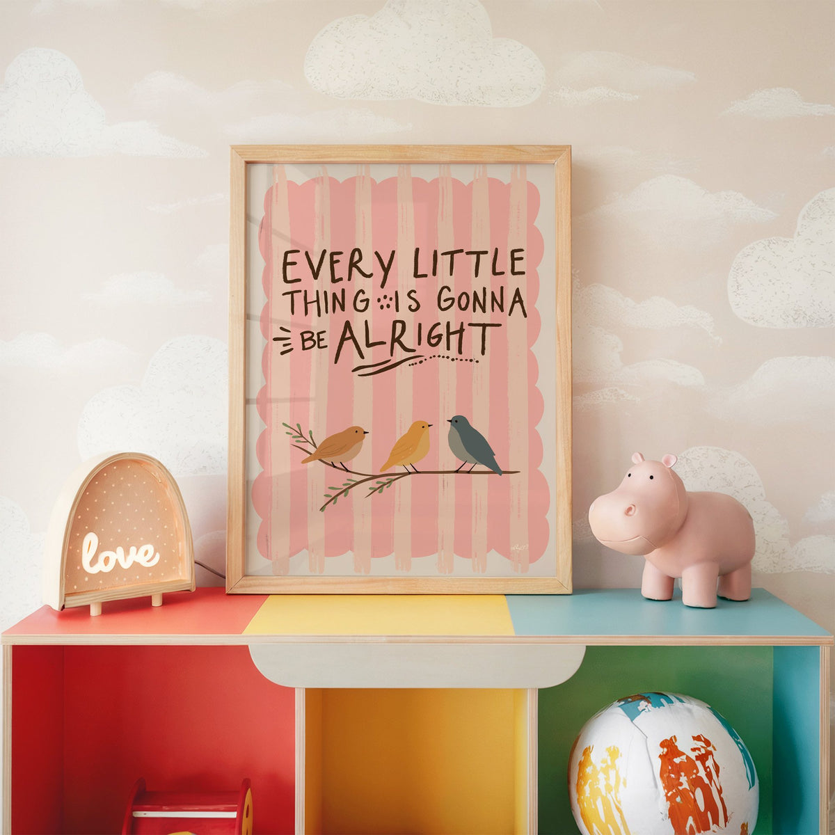 Every little thing birds quote nursery print in an oak frame on a rainbow toy shelf against cloud wallpaper
