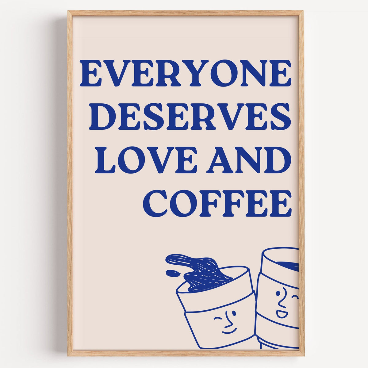 Everyone Deserves Love and Coffee print in a light oak frame on a plain white wall