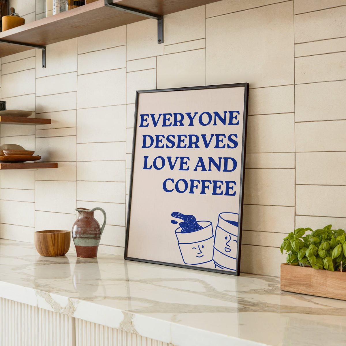 Everyone Deserves Love and Coffee print in a black frame leaning on a marble counter in a tiled kitchen