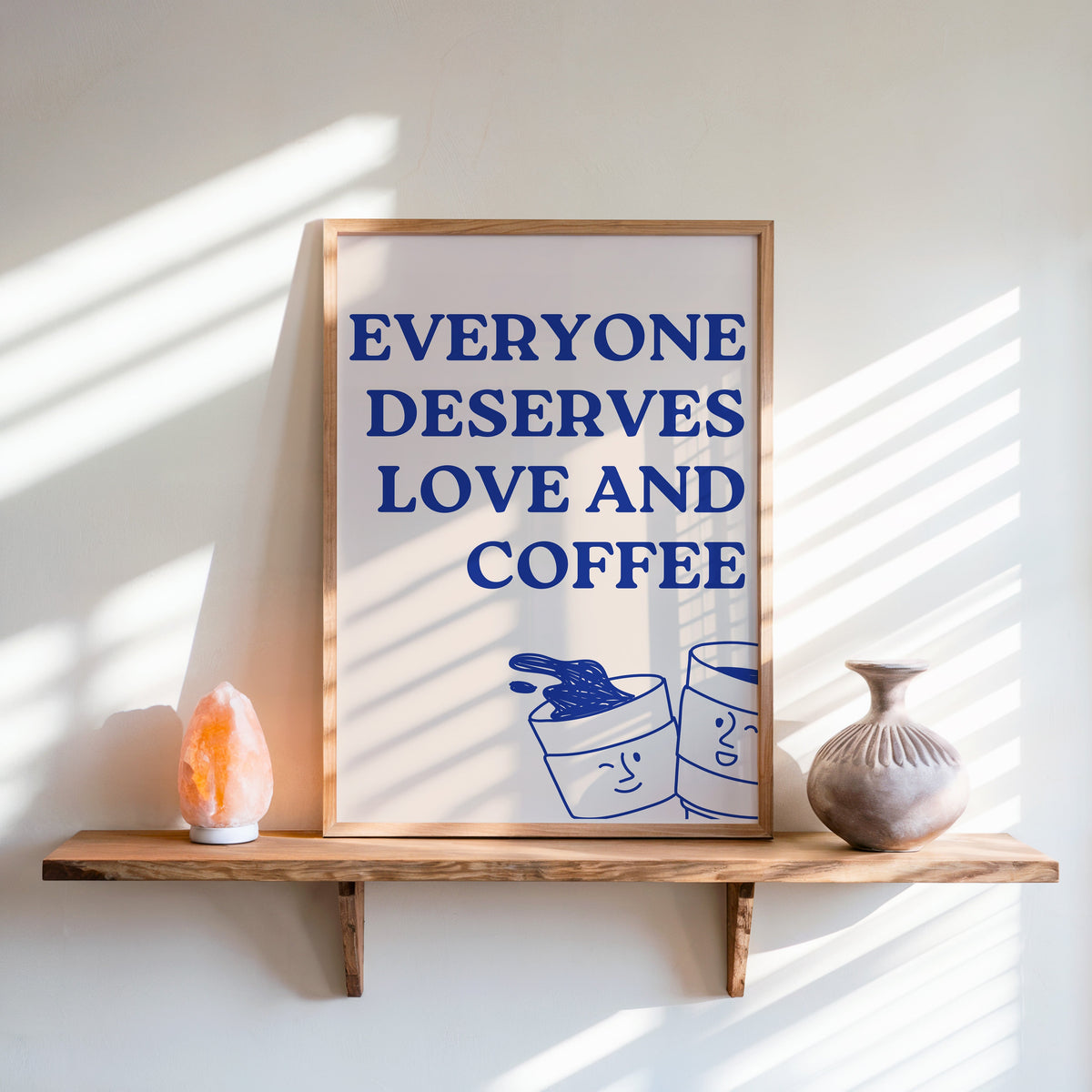 Everyone Deserves Love and Coffee print in an oak frame on a live-edge shelf beside a salt lamp