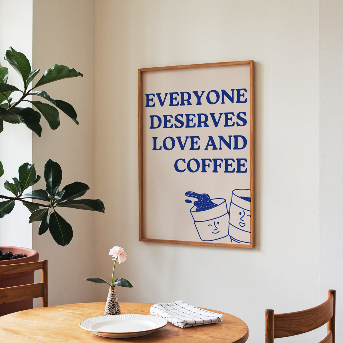 Everyone Deserves Love and Coffee print in a walnut frame above a round table beside a fiddle-leaf fig