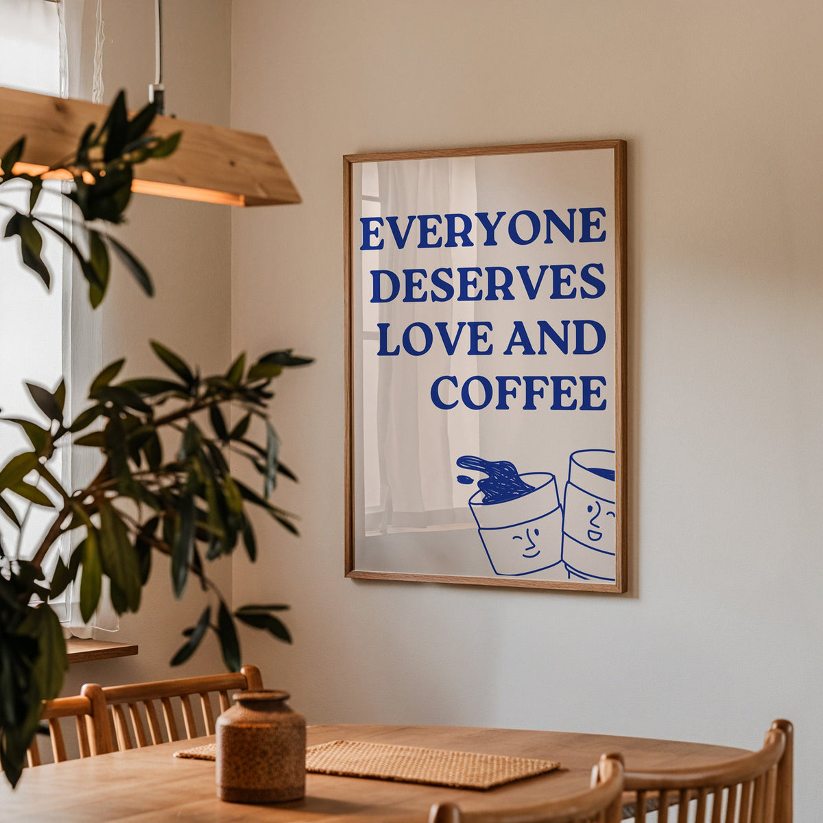 Everyone Deserves Love and Coffee print in a walnut frame above a dining table with olive branches
