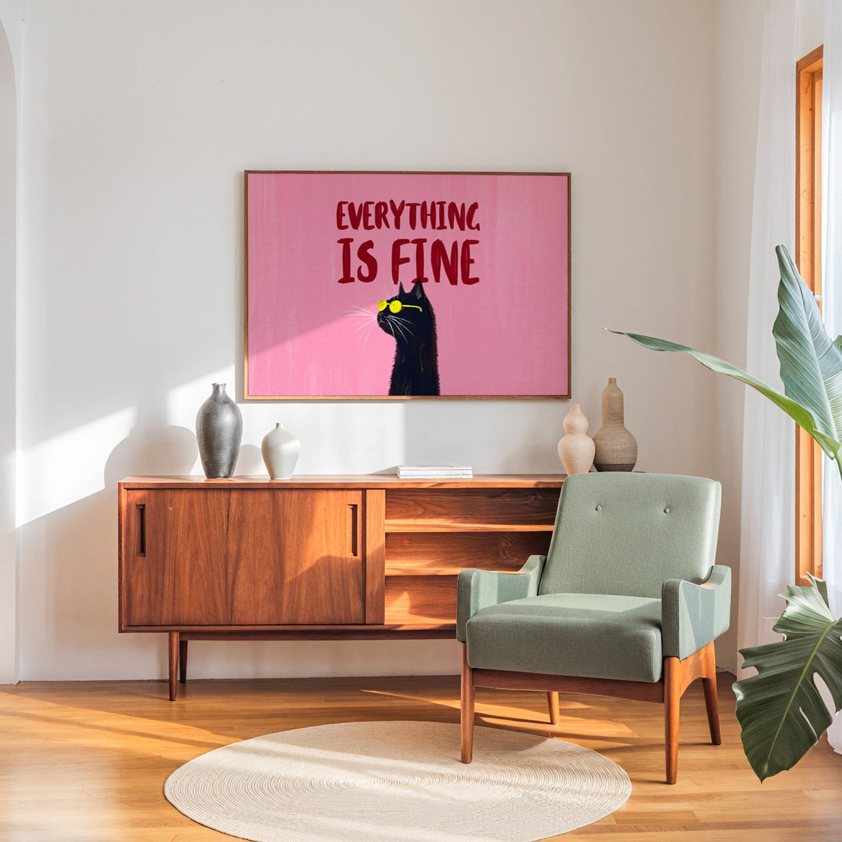 Black cat quote print in a walnut frame above a sideboard beside a sage armchair