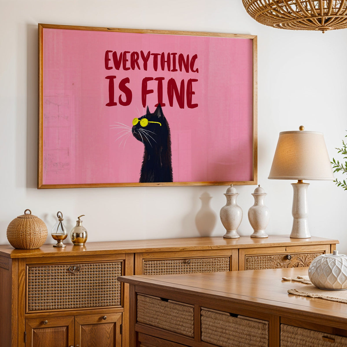 Funny black cat typography print in an oak frame above a cane sideboard with a table lamp