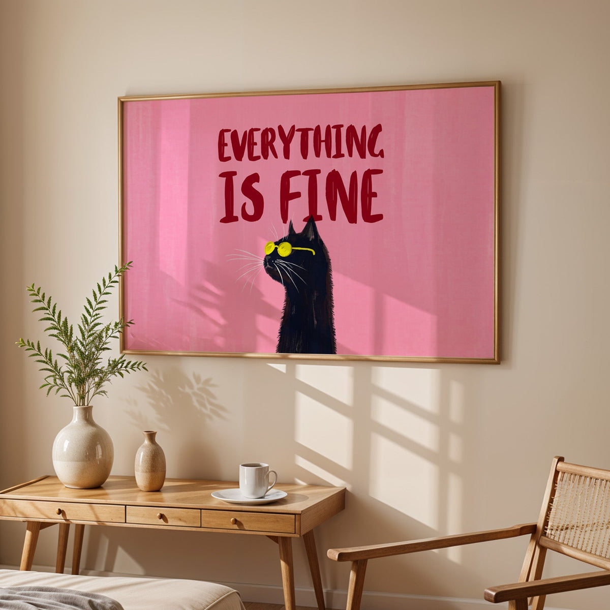 Pink cat in sunglasses print in an oak frame above a sunlit desk with a cane chair