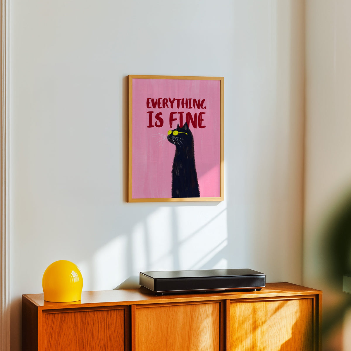 Everything Is Fine cat poster in a light oak frame above a teak sideboard with a yellow lamp