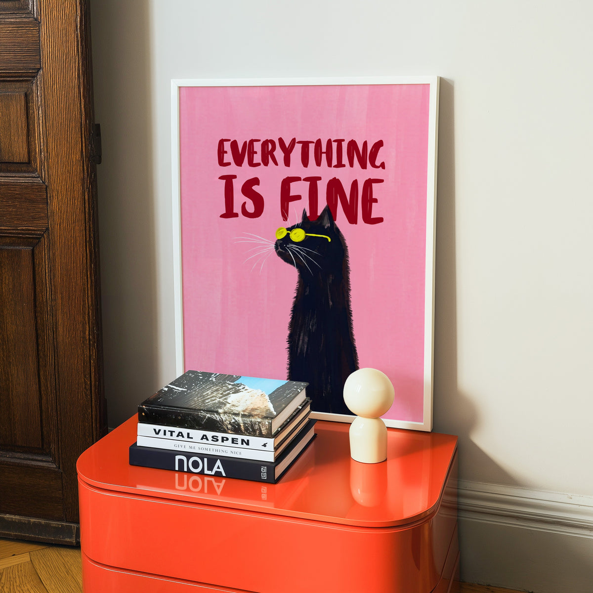 Funny cat in sunglasses print in a white frame on a glossy orange cabinet with books