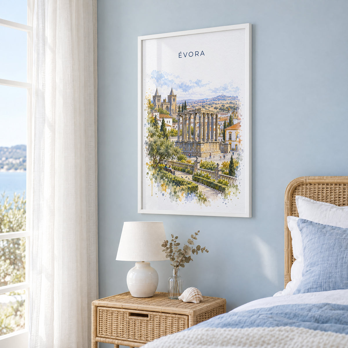 Évora watercolor print in a white frame on a pale blue wall beside a rattan bed in a coastal bedroom