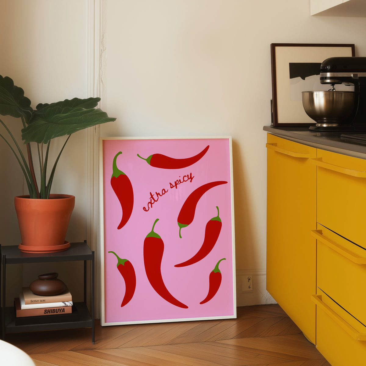 Chilli pepper print in a white frame leaning on parquet beside a bright yellow kitchen