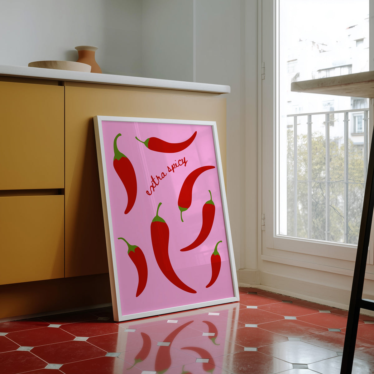 Chilli pepper print in a white frame against yellow cabinets on a red tiled floor