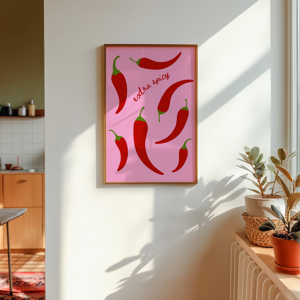 Chilli pepper print in a gold frame in sunlight with plants on the ledge and a kitchen beyond