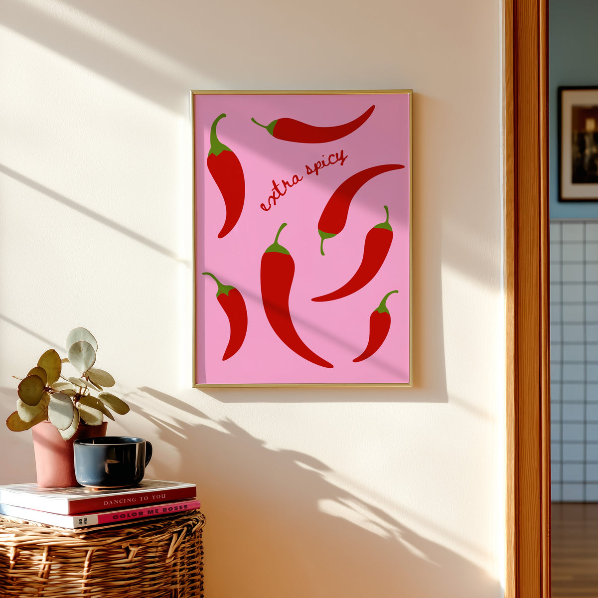 Chilli pepper print in a gold frame above a basket of books and a pilea plant