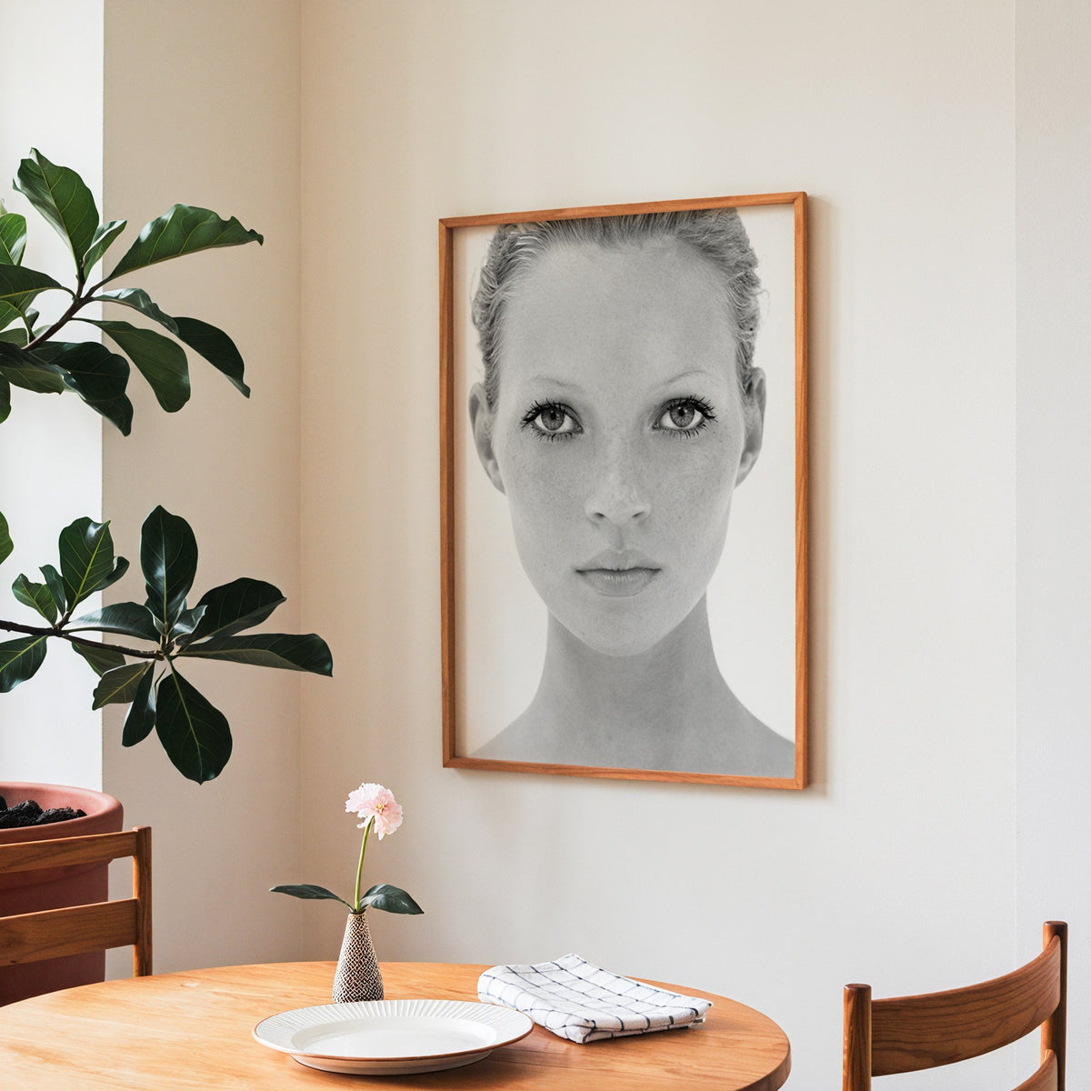 Bright face closeup with dark lashes print in a teak frame above a round wooden dining table