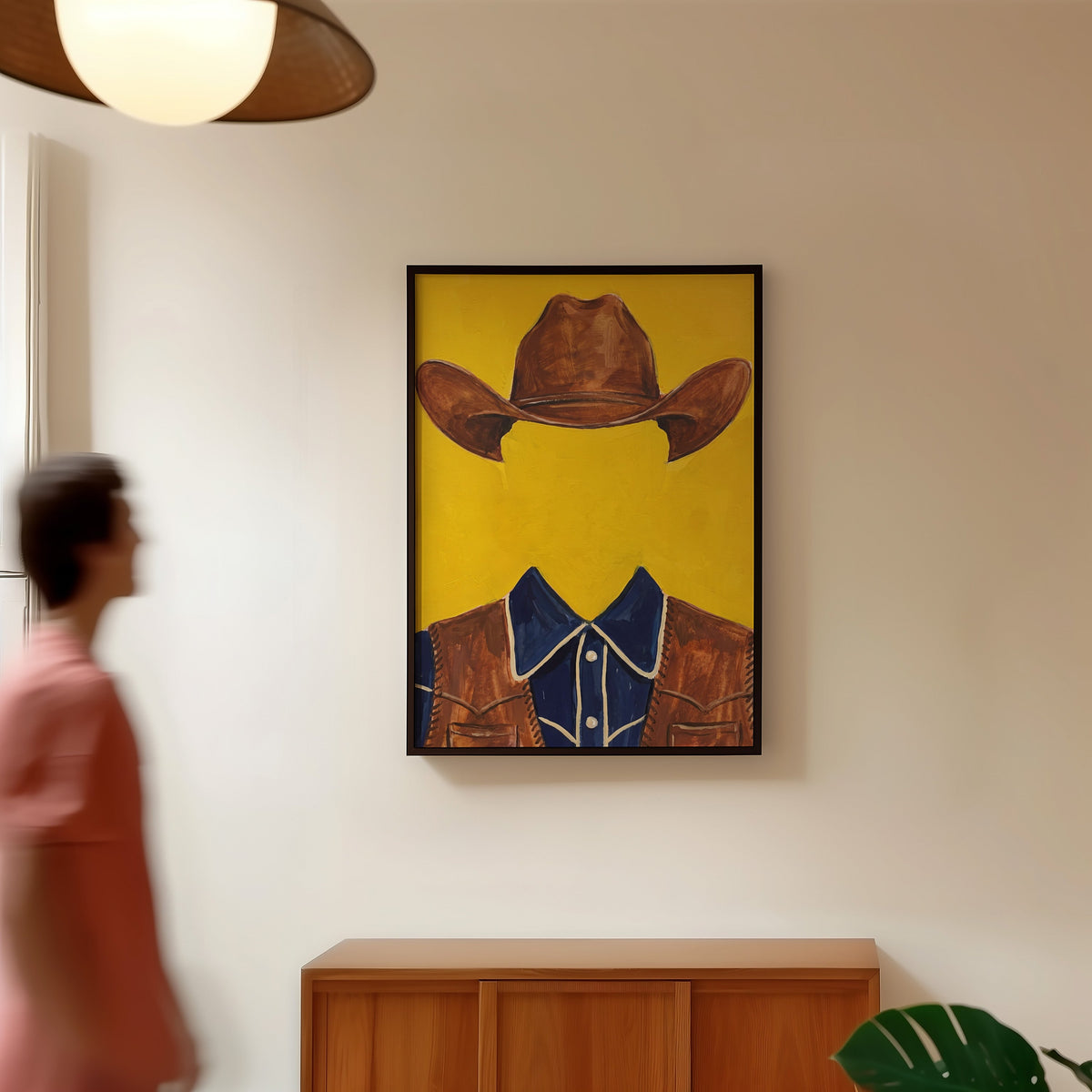 Yellow cowboy print in a black frame in a hallway under a rattan pendant