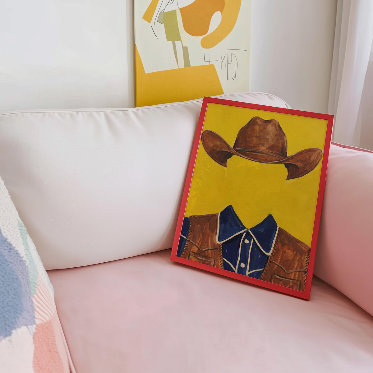 Western shirt and hat print shown in a red frame leaning on a blush pink sofa