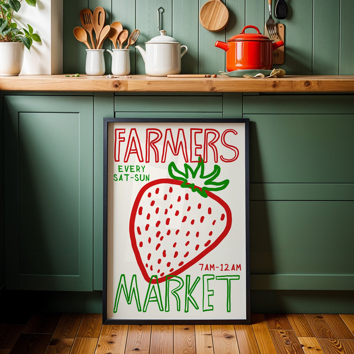 Farmers market strawberry print in a black frame against sage green kitchen cabinets