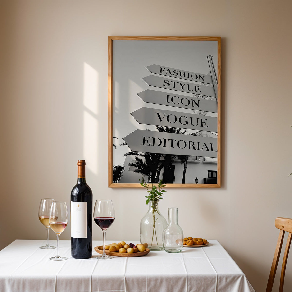 Street signpost with fashion words above palm trees print in an oak frame above a table set with red wine and glasses