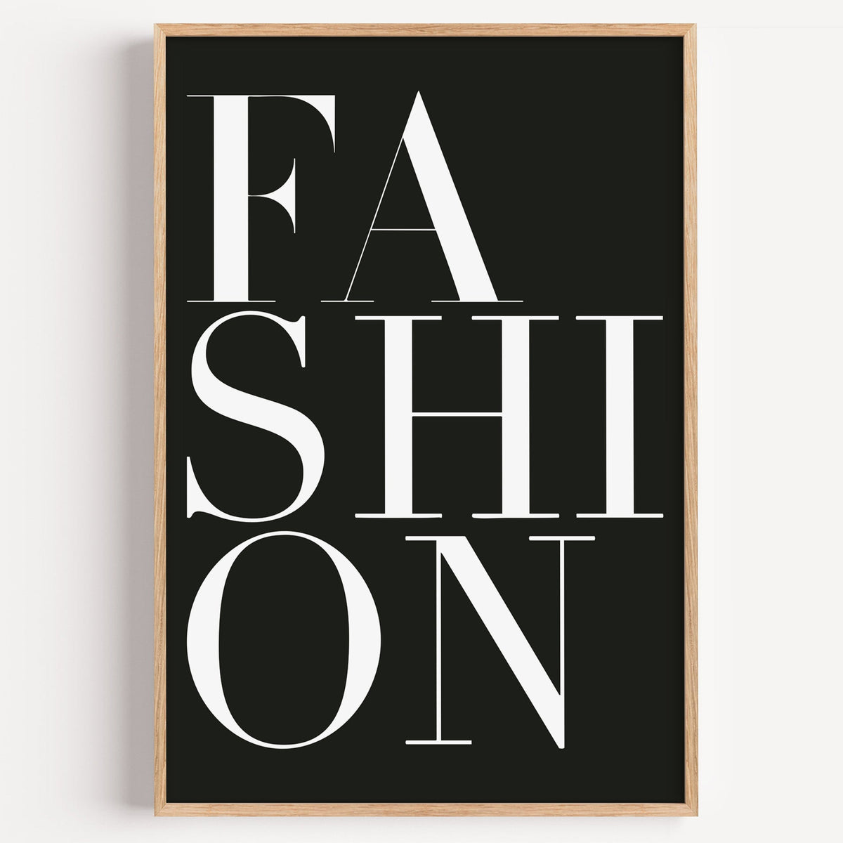 Stacked serif FASHION lettering on charcoal print in a light oak frame on a plain white wall