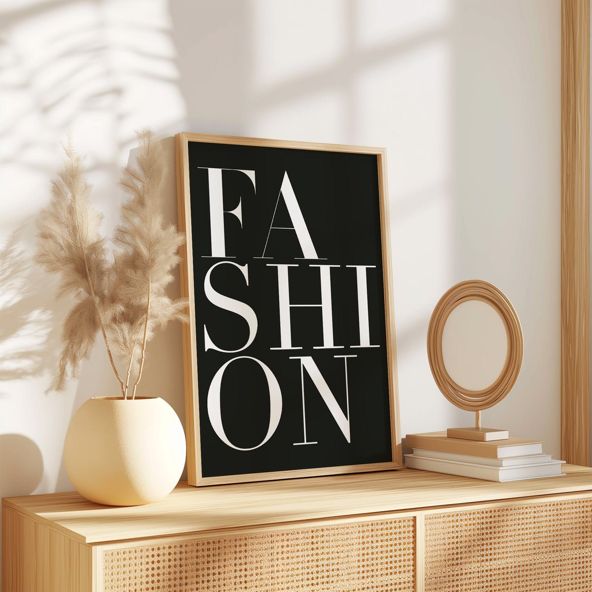 Stacked serif FASHION lettering on charcoal print in an oak frame on a rattan sideboard beside pampas grass