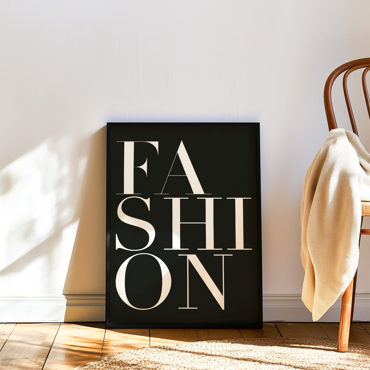 Stacked serif FASHION lettering on charcoal print in a black frame leaning on a wood floor beside a bentwood chair