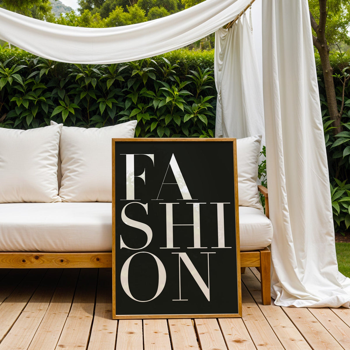 Stacked serif FASHION lettering on charcoal print in an oak frame on an outdoor daybed under white drapes