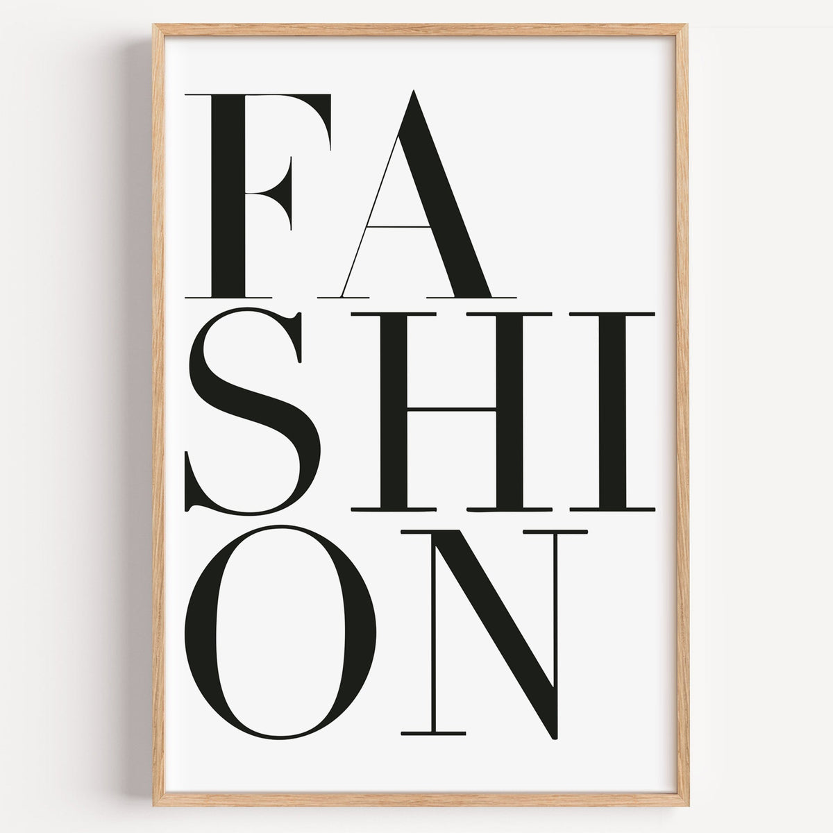 Stacked serif FASHION lettering on white print in a light oak frame on a plain white wall