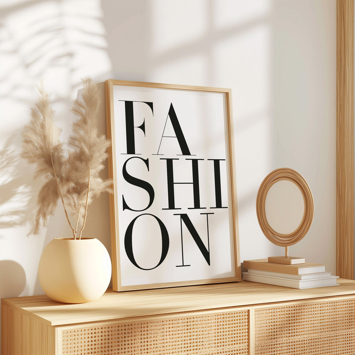 Stacked serif FASHION lettering on white print in an oak frame on a rattan sideboard beside pampas grass