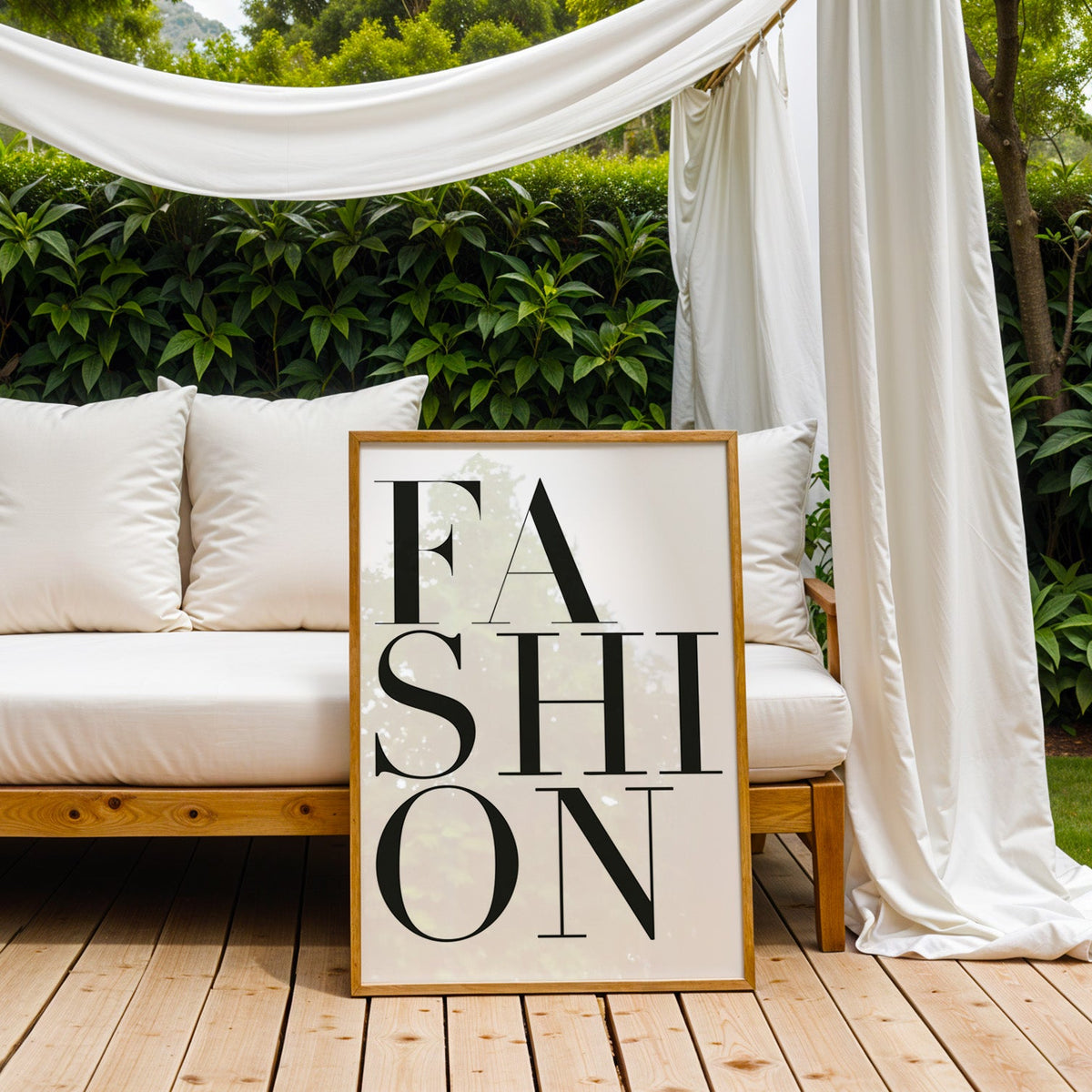 Stacked serif FASHION lettering on white print in an oak frame on an outdoor daybed under white drapes