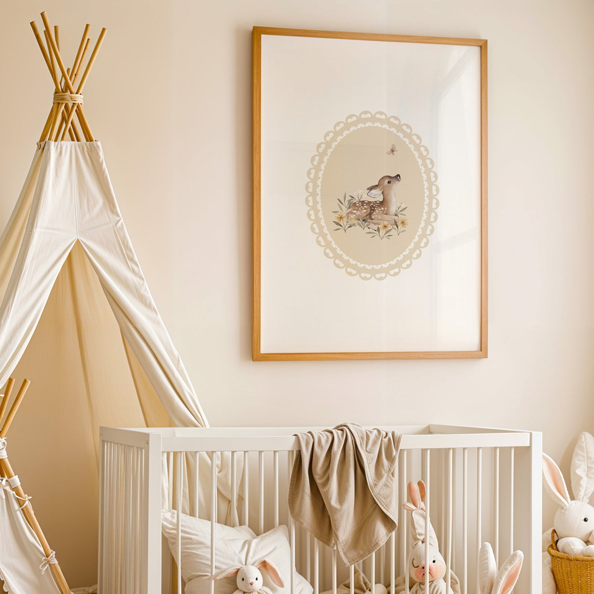 Fawn watching a butterfly in a lace oval nursery print in an oak frame above a white crib beside a canvas teepee