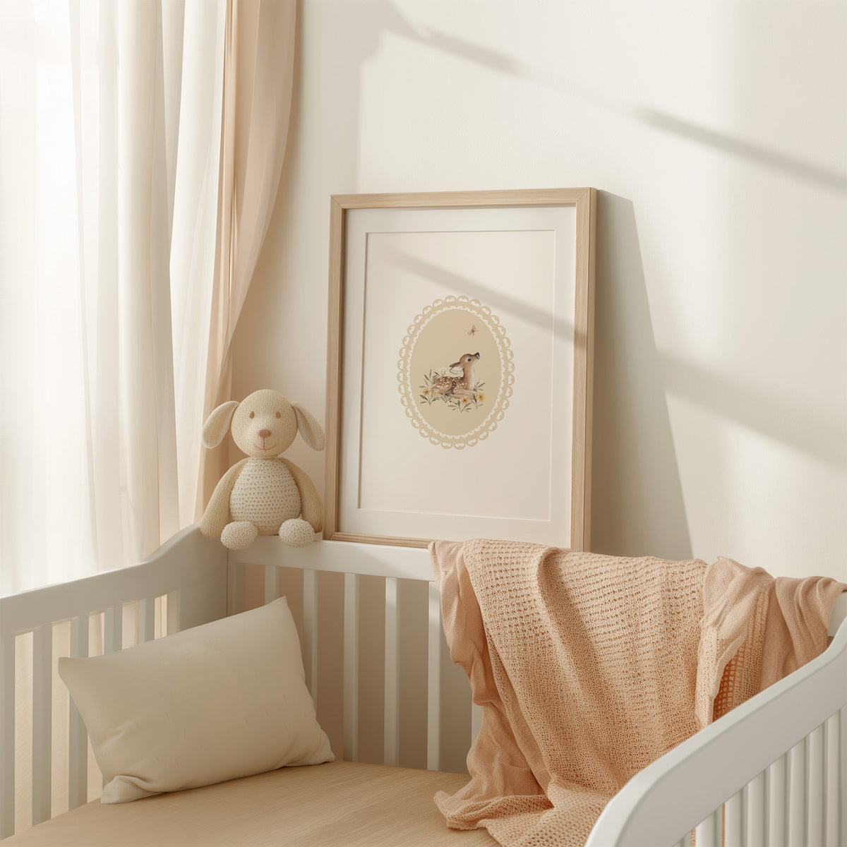 Fawn watching a butterfly in a lace oval nursery print shown in an oak frame with a white mat on a crib rail