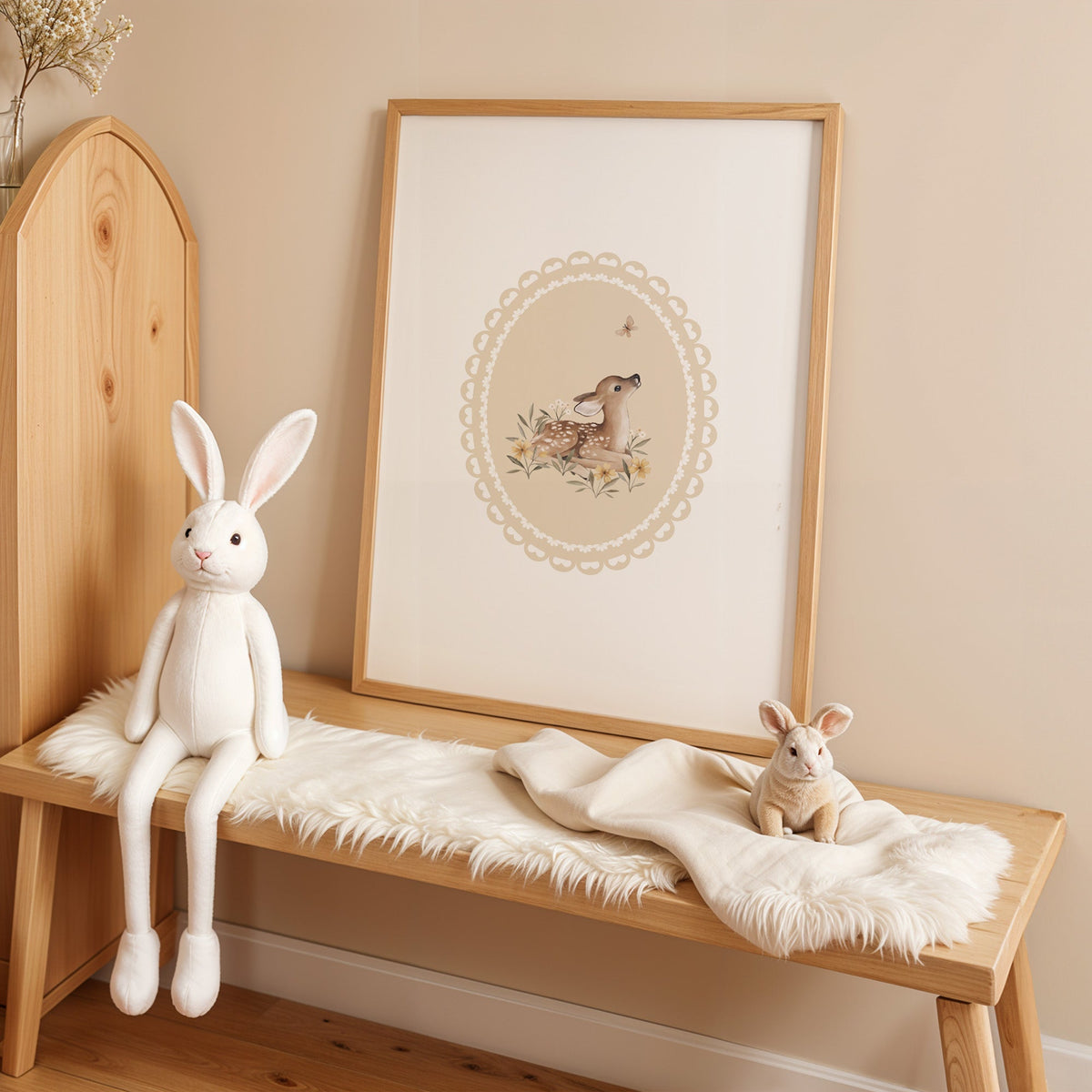 Fawn watching a butterfly in a lace oval nursery print in an oak frame on a sheepskin bench beside a white plush bunny