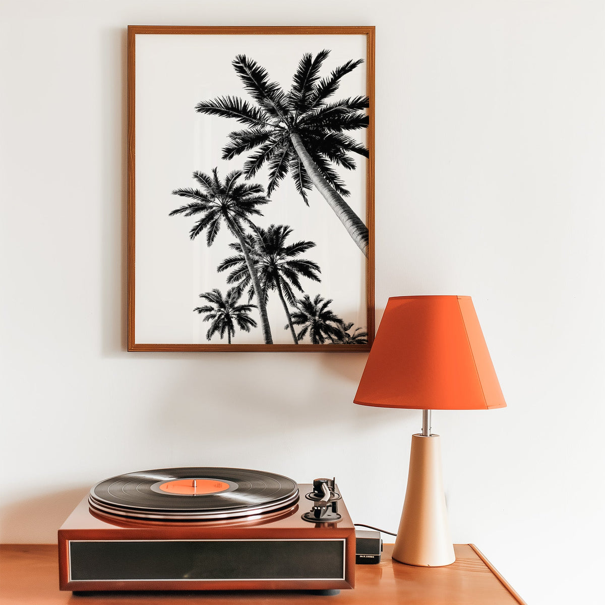 Feather leaf palms on a white sky print in a walnut frame above a record player and orange lamp