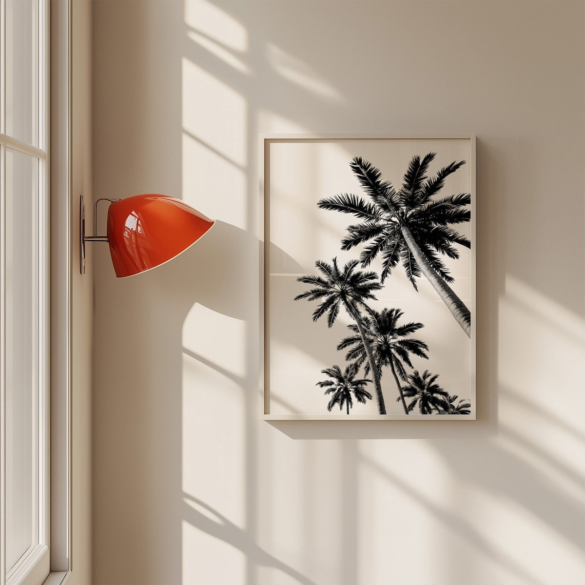 Feather leaf palms on a white sky print in a white frame on a sunlit wall beside a red sconce