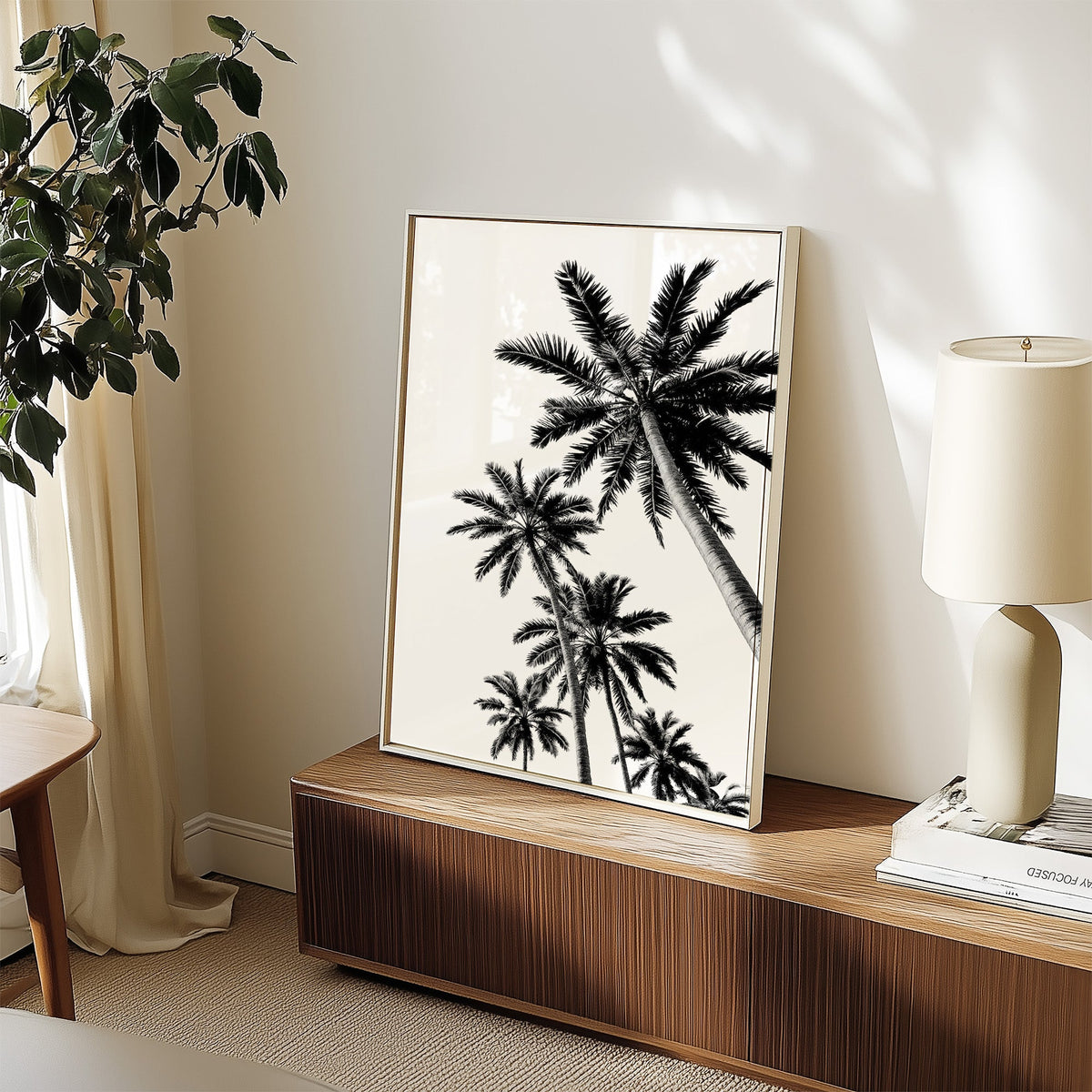 Feather leaf palms on a white sky print in a white frame on a walnut sideboard beside a ceramic lamp
