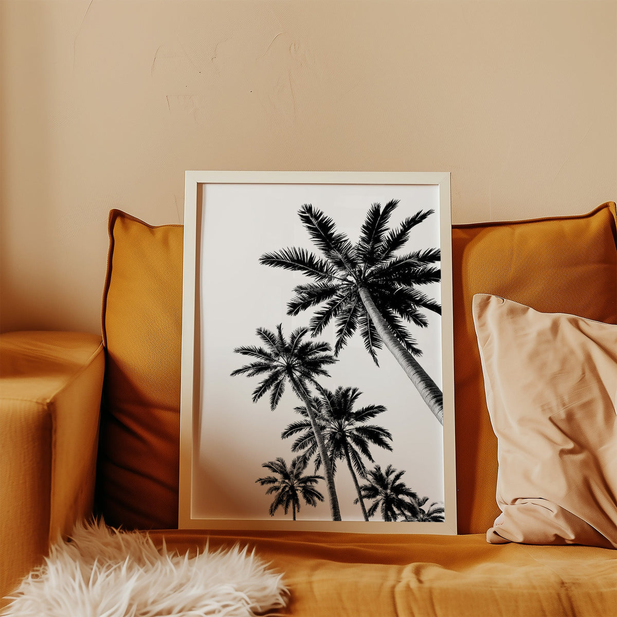 Feather leaf palms on a white sky print in a white frame leaning on a mustard velvet sofa