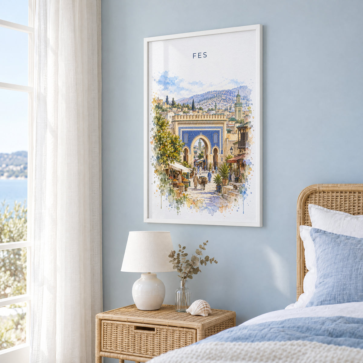 Fes, Morocco watercolor print in a white frame on a pale blue wall beside a rattan bed in a coastal bedroom